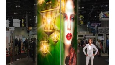 Trade show booth: green panel with glowing lanterns and a woman's portrait; a presenter stands beside it.