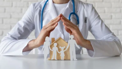 Doctor with stethoscope protecting a paper-family and wooden house, symbolizing family health insurance/care