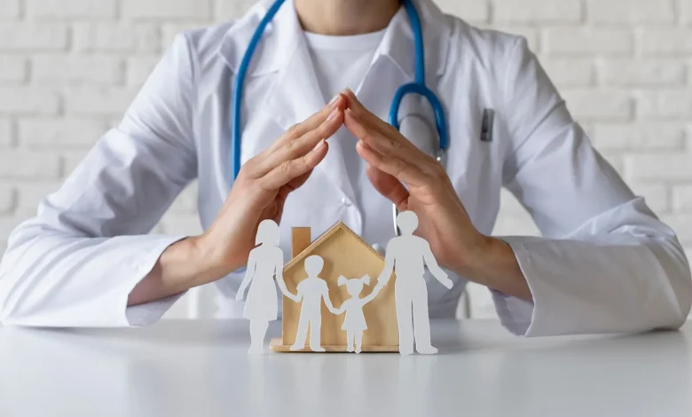 Doctor with stethoscope protecting a paper-family and wooden house, symbolizing family health insurance/care